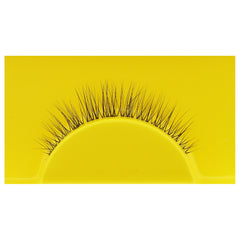 A single Boldface Lashes - Short and Sweet false eyelash rests on a vibrant yellow background. This cruelty-free beauty by Boldface showcases fine, evenly spaced black fibers arranged in a natural curve, enhancing the appearance of eyelashes when worn while ensuring this accessory is both captivating and kind.