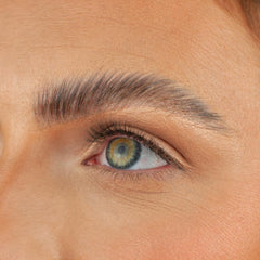 A close-up of a person's left eye showcases green and hazel hues, framed by thick, well-groomed eyebrows and enhanced with cruelty-free makeup. Boldface's