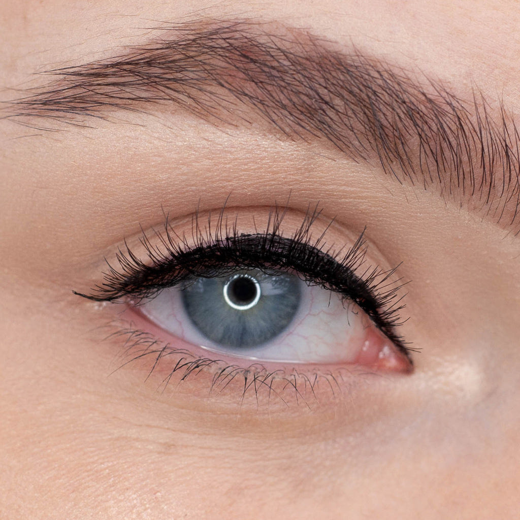A close-up image of a blue eye with long eyelashes showcases the Ardell Naked Lashes 420 Multipack for added allure. The eyelid is adorned with black eyeliner, and the eyebrow is neatly groomed. The eye gazes directly ahead, highlighting the intricate details of this cruelty-free lash look from Ardell.