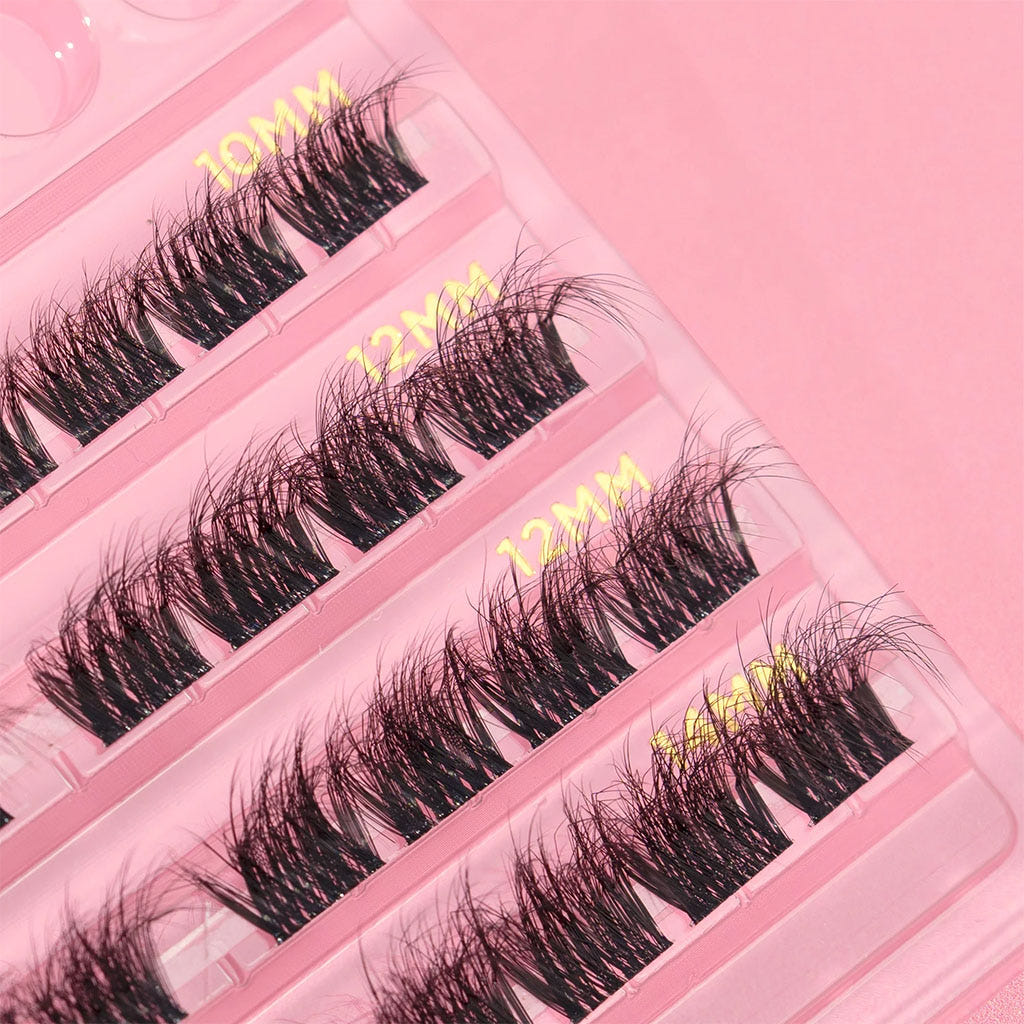 A close-up image features a pink case filled with Doll Beauty Individual Lash - 02 Full options, highlighting fluffy lashes in assorted lengths of 10mm, 12mm, and a striking 44mm. Each row is meticulously arranged to create a captivating appearance, perfectly complemented by the pink background that enhances the selection of glamorous lashes within.