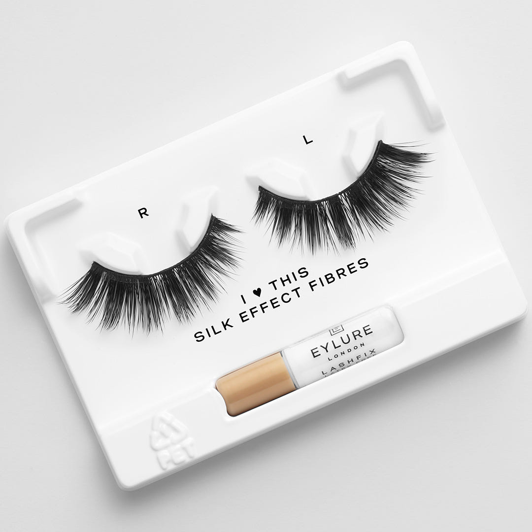 A set of the Eylure Most Wanted Lashes - I Heart This, featuring labels "R" and "L," sits on a white tray accompanied by a small bottle of adhesive. The tray displays the text "I ♥ THIS SILK EFFECT FIBRES" next to the Eylure logo. These lashes offer a luxurious feel and are cruelty-free.