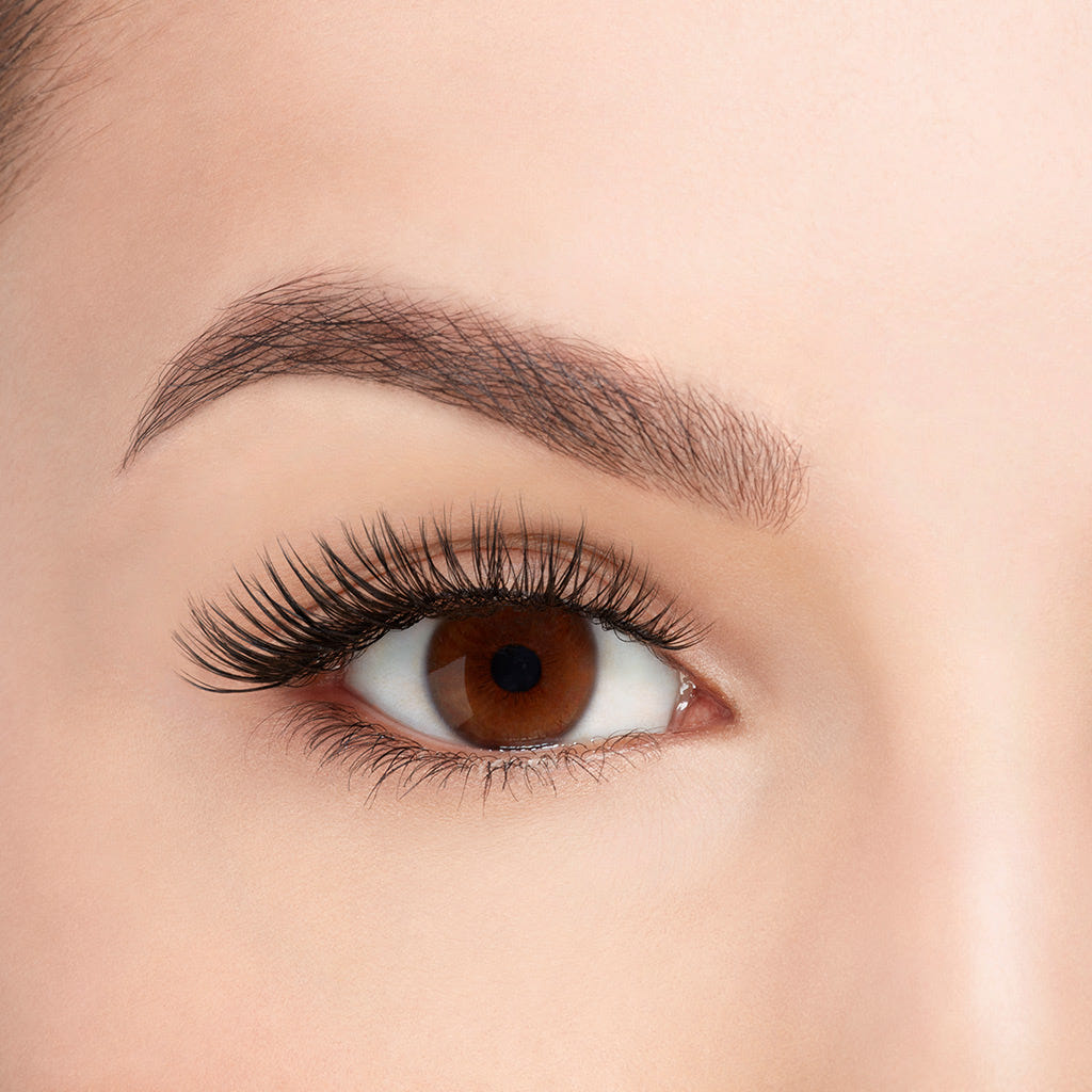 A close-up of a woman's eye showcases her long eyelashes accentuated by Ardell Faux Mink Lashes Black Demi Wispies from the multipack. Her neatly groomed eyebrows and smooth skin complement the striking makeup and highlight her natural features.