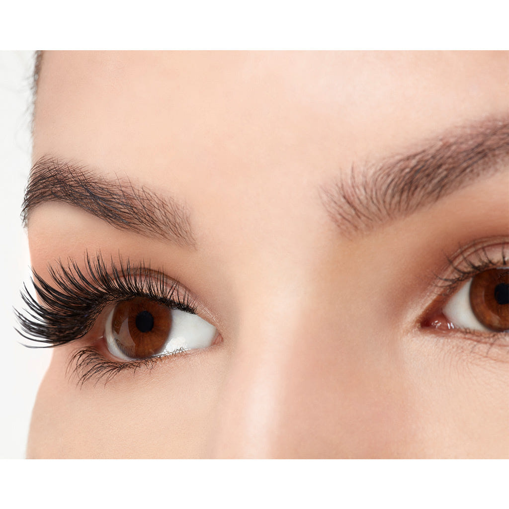 Close-up of a woman's eyes, featuring Ardell Faux Mink Lashes Black Demi Wispies from Ardell that add length and volume to her left eye. Her eyebrows are well-groomed, and the skin appears smooth and clear. Light makeup enhances her natural beauty, while the brown eyes mesmerize with their allure.