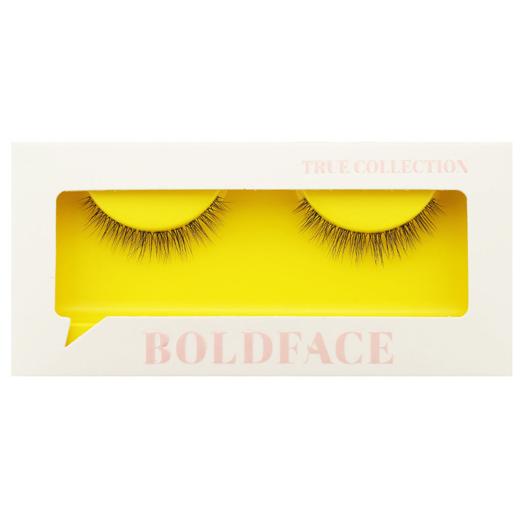The Short and Sweet false eyelashes by Boldface are presented in a white rectangular box featuring a clear display window. The cruelty-free lashes are highlighted against a vibrant yellow backdrop. The packaging is adorned with "BOLDFACE" and "TRUE COLLECTION" in light pink lettering.