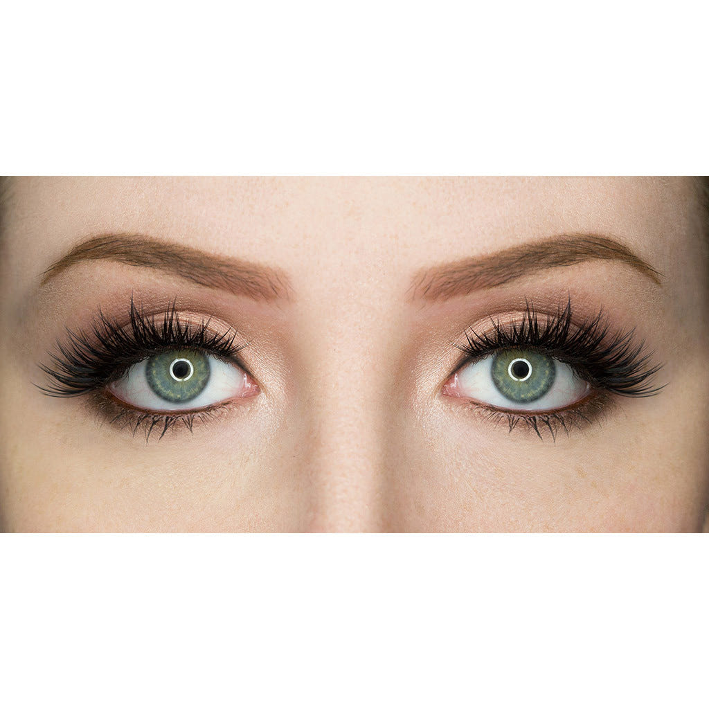 A close-up of a person's eyes with green irises. The person is wearing dramatic, long false eyelashes from House of Lashes - Iconic and has well-groomed, dark eyebrows. The eyes appear to be brightly lit, reflecting circular light rings in the pupils. The surrounding skin is smooth and flawless.